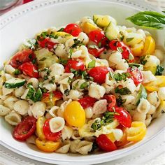 a white bowl filled with pasta salad topped with cherry tomatoes and green leaves on top