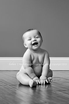 a smiling baby sitting on the floor with his mouth open and eyes wide open in black and white