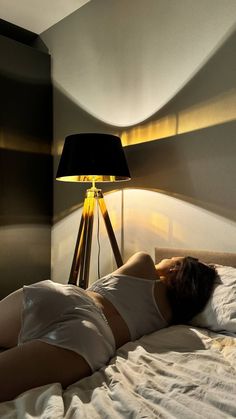 a woman laying in bed next to a lamp on the side of her head and body