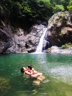 two people in the water near a waterfall