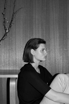 a black and white photo of a woman sitting on a bench in front of a wall