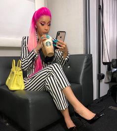 a woman with pink hair sitting on a couch holding a cell phone and looking at her phone