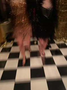 two women in black and white dresses are dancing on a checkered floor with sparkles