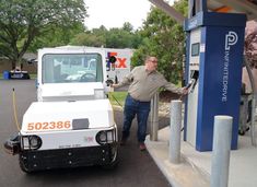 a man standing next to a white truck at a gas station with his hand on the fuel pump