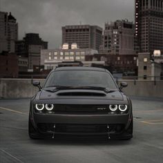 the front end of a black car parked in a parking lot with tall buildings behind it