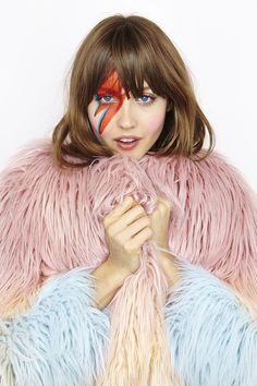 a woman with her face painted like a bird and holding a piece of yarn in front of her face