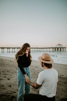 a man holding the hand of a woman at the beach with a pier in the background