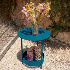 a blue table with jars and flowers on it next to a rock wall, in the shade