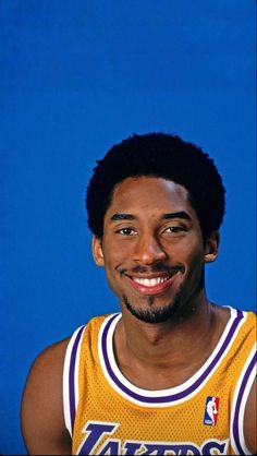 a smiling man in a lakers jersey is posing for a photo against a blue background