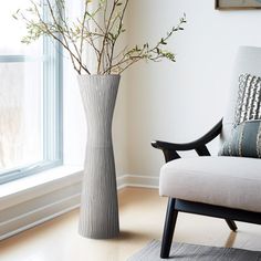 a living room with a couch, chair and vase on the floor next to a window