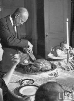 an old black and white photo of people at a dinner table with turkey on the table