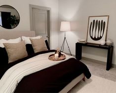 a bedroom with black and white bedding, brown pillows and a round mirror on the wall