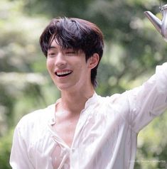 a young man is smiling and holding his hands up in the air while wearing a white shirt