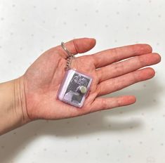 a person's hand holding a small square keychain with a photo on it