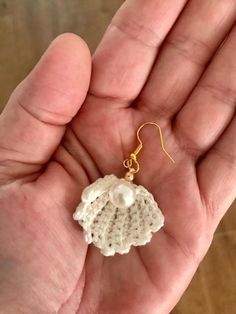 a hand holding a small white crochet earrings with pearls on it's end