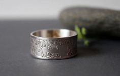 a silver ring sitting on top of a table next to a leafy green plant