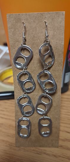 two pairs of metal earrings sitting on top of a wooden table next to a card