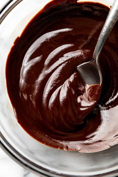 a spoon is in a bowl filled with chocolate frosting and melted chocolate on the side