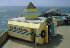 the giant camera is on display at the edge of the cliff by the ocean with people standing around it