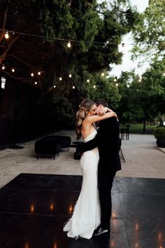 a bride and groom embrace on the dance floor at their wedding reception in front of string lights