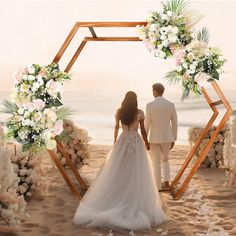 a bride and groom are walking down the beach towards the ocean in front of their wedding arch