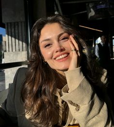 a woman sitting at a table smiling and holding her hand to her face