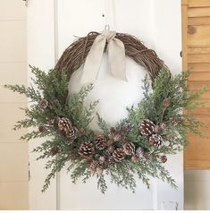 a wreath with pine cones and greenery hanging on a door