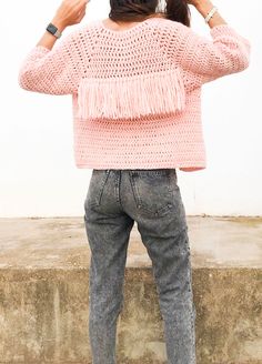 a woman standing on concrete with her back to the camera and wearing a pink sweater