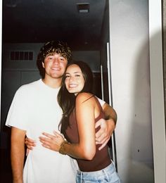 a man and woman standing next to each other in front of a mirror with their arms around each other