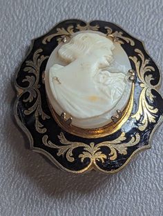 "Antique Shell Cameo & Black Enamel Brooch Pin HALLMARKS Unmarked. MEASUREMENTS 1 3/8\" x 1 5/8\".               MATERIALS Shell, Black Enamel, Gold Gilt. CONDITION In very good condition with minimal wear on gold gilt, please use all pictures as part of item's description. Turn of the Century Edwardian era Mourning Cameo brooch featuring carved shell center of classic Roman or Grecian lady in profile prong set in Black Enamel frame with ornate Gold Gilt designs. This is a very unique cameo. Cam Victorian Brooches With Intricate Design, Victorian Brooches For Ceremonial Occasions, Ornate Oval Brooch For Formal Occasions, Ornate Oval Brooches For Formal Occasions, Victorian Style Cameo Brooch For Weddings, Victorian Cameo Brooch For Wedding, Antique Medallion Brooch For Wedding, Victorian Oval Filigree Brooches, Victorian Engraved Brooches For Formal Wear