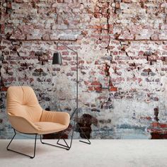 an orange chair sitting in front of a brick wall with a black lamp on it