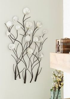 a metal wall sculpture with white flowers and branches in front of a fireplace mantel