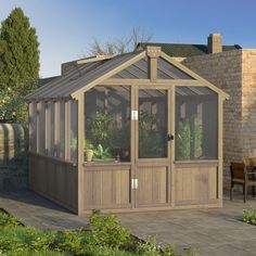 a small wooden greenhouse with glass doors and windows on the sides, in front of a brick building