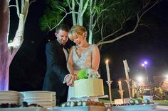 a bride and groom are cutting their wedding cake at the reception table with lit candles in the background