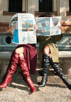 two women sitting on a bench reading the paper while wearing knee high boots and over - the - knee boots