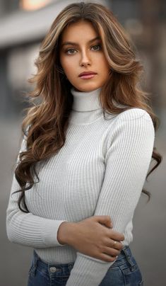 a woman with long brown hair wearing a white turtle neck sweater and jeans is posing for the camera