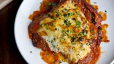 a white plate topped with lasagna covered in sauce and parmesan cheese