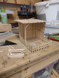 a wooden house sitting on top of a workbench in a workshop with tools