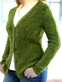 a woman wearing a green cardigan sweater and jeans standing in front of a window