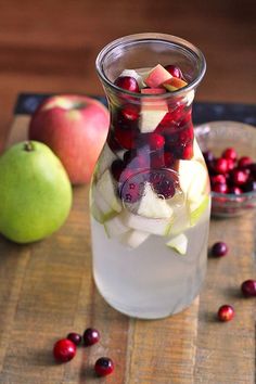 a pitcher filled with fruit and ice on top of a wooden table next to apples