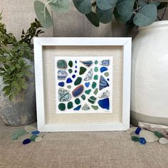 a white frame sitting on top of a table next to a vase filled with plants