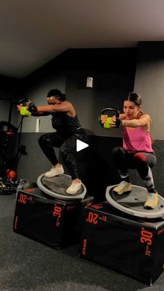 two people doing exercises on exercise mats in a room with black walls and gray carpet