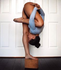 a woman doing a handstand on top of a block in front of a door