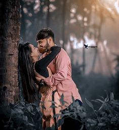 a man and woman standing next to each other near a tree in the middle of a forest