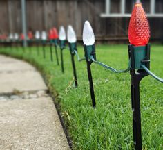 several red and white christmas lights on black poles in the grass near a fenced yard