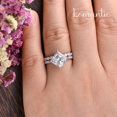 a woman's hand with a wedding ring on it and flowers in the background