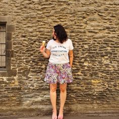 a woman standing in front of a stone wall holding an ice cream cone with the words ice cream appreciation society written on it