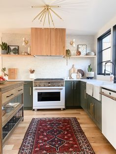 a kitchen with green cabinets, white appliances and a red rug in front of the stove