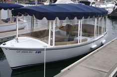 a white boat with a blue cover docked at a dock next to other boats in the water