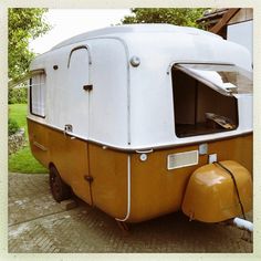 an old yellow and white trailer parked on the side of a road in front of a house